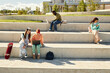 © Seventyfour - Wide angle shot of students of diverse ethnicity sitting on concrete seats of amphitheater in park using laptops and phones surfing net after classes outdoors