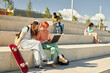 © Seventyfour - Smiling teenage male skateboarder and redhead girl in bright outfit having fun while using laptop together on concrete seat of amphitheater in park