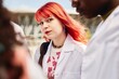 © Seventyfour - Portrait of young female med student with brightly dyed red hair smiling and looking at camera while standing with classmates outdoors on sunny day, copy space