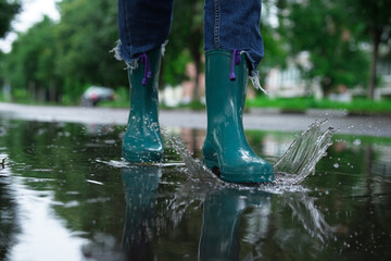 Wall Mural - Woman wearing turquoise rubber boots walking in puddle outdoors, closeup