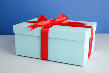 Poster - Gift box with red satin bow on color background, closeup