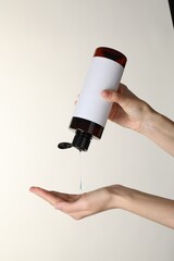 Poster - Woman pouring shampoo onto hand on beige background, closeup