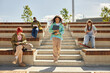 © Seventyfour - Full length shot of multiethnic teenage girl with curly hair walking down stairs of amphitheater, where students casually learning reading books and using phones on sunny day outside