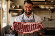 © Kitta - A butcher proudly displays a massive prime rib, a testament to quality and craftsmanship. The rich marbling and bone-in cut promise a delicious culinary experience.