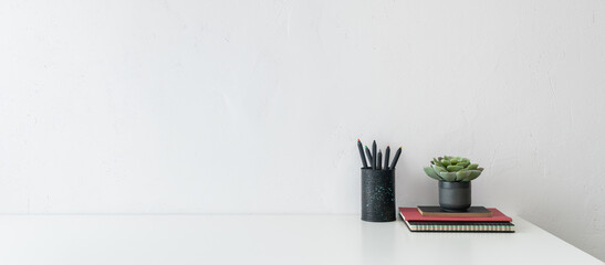 Creative desk with an empty space, desk objects, office supplies, books, and plant on white wall background.	
