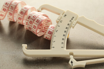 Wall Mural - Plastic body fat caliper and measuring tape on grey table, closeup