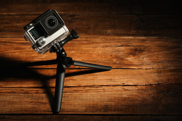 Canvas Print - Modern action camera and tripod on wooden surface. Space for text