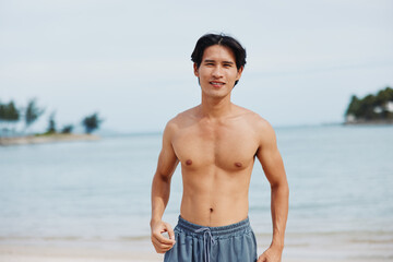 Wall Mural - Happy Asian Man Enjoying Summer Vacation on Tropical Beach, Smiling with Muscular Torso and Sexy Abs, Relaxing in the Sun on Sandy Island