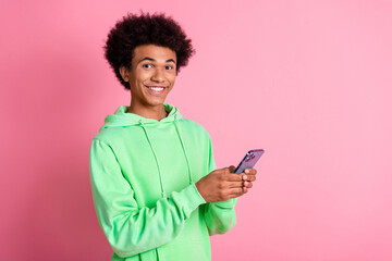 Wall Mural - Photo of nice young man use phone empty space wear green hoodie isolated on pink color background