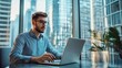 © Premreuthai - A focused man works on his laptop in a modern office with a stunning city view, capturing productivity and urban lifestyle.