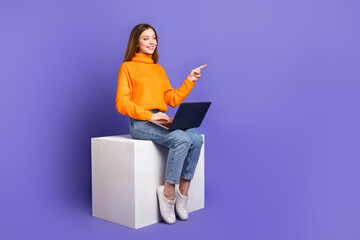 Canvas Print - Photo of teen girl in orange turtleneck and jeans using laptop pointing finger her first website mockup isolated on purple color background