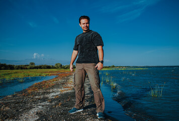 Poster - Young handsome man standing on lake shore on summer day