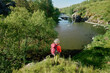 © pressmaster - Beautiful landscape with wide river flowing among banks with green trees and other vegetation and female hiker standing by waterside