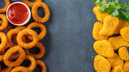 Wall Mural - Fried onion rings and chicken nuggets on black background