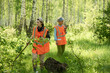 © pressmaster - Young and mature female volunteers or lifeguards in acid orange reflective vests moving along forest and seeking for lost tourists