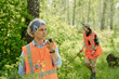 © pressmaster - Confident mature female rescuer speaking on walkie-talkie while reporting about accident with tourist in the forest against other lifeguard