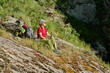 © pressmaster - Side view of tired mature female hiker having rest on mountain among green grass during trip on sunny summer day
