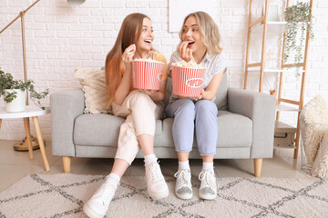 Young sisters eating popcorn on sofa at home