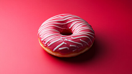 A delicious donut cake covered in pink chocolate icing with white chocolate drizzled in a zigzag pattern. It stands out against a vibrant red background.