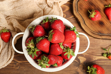 Colander and board with fresh strawberries on wooden background