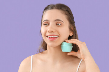 Wall Mural - Young woman with jar of facial cream on lilac background, closeup