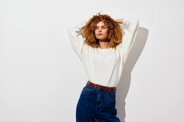 Stylish young woman with curly hair in casual attire against a minimalistic white background, exuding confidence and modernity in a relaxed pose