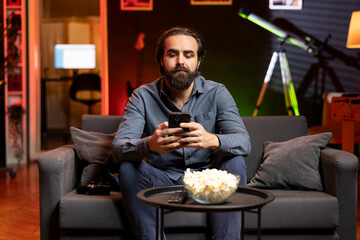 Wall Mural - Man taking break from playing videogame to text friends in neon lit room, holding smartphone. Gamer in apartment living room pausing game to speak with mates on mobile phone