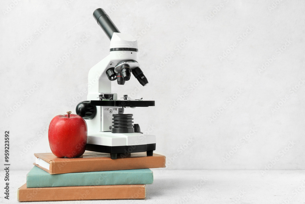 Microscope, school books and apple on light background