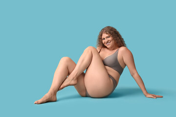 Wall Mural - Beautiful young happy body positive woman in stylish underwear sitting on blue background