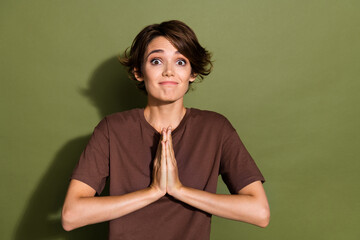 Poster - Portrait of excited pleading girl with short hair wear oversize t-shirt hold palms together praying isolated on green color background