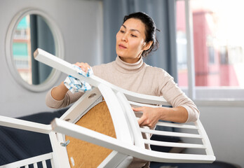 Hardworking asian woman wipes a chair with a rag, tidying up the apartment