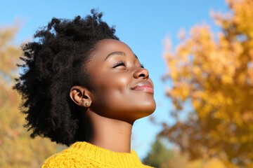 Wall Mural - African woman wearing yellow knitted sweatshirt in autumn park at sunny day