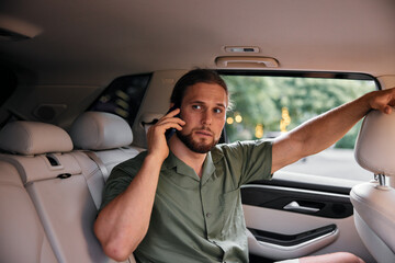 Man in a car making a phone call, wearing a green shirt, looking thoughtful Bright interior with a blurred outdoor background