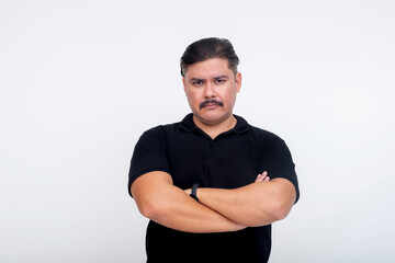 A middle-aged man with a mustache looking sternly, arms crossed with steely intimidating eyes. Wearing a black collared shirt. Set against a white background.