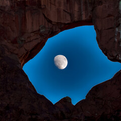 Sticker - A full moon rises through a natural arch in a rocky landscape, casting a soft, ethereal glow.

