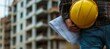 © adri - Construction worker holding blueprints and a hard hat.