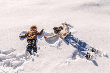 a happy winter family, mother and son lying in the snow now, playing and having fun together.