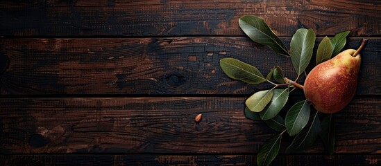 A single juicy ripe pear with leaves rests on a dark vintage wooden background Top view copy space