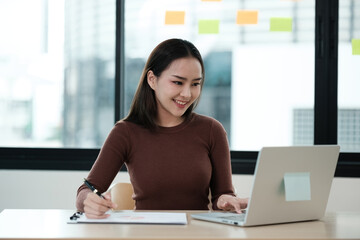 A woman is sitting at a desk with a laptop and a piece of paper