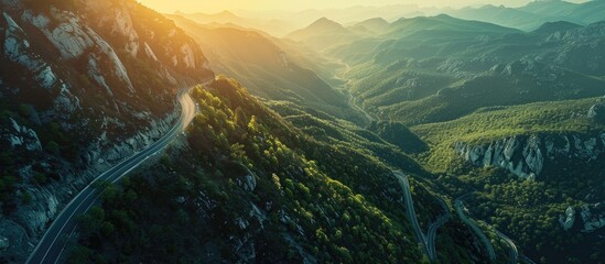 Poster - Aerial perspective of a mountain road at sunrise with a winding asphalt path cutting through the mountain range and lush green forest. Copy space image. Place for adding text and design
