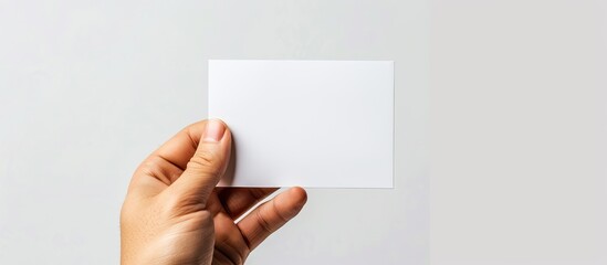 Wall Mural - An empty white paper card is held in hand against a white background. Copy space image. Place for adding text and design