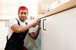 © artitwpd - Asian professional plumber man work in a uniform fixing a broken water pipe problem under the sink in the client kitchen house. Indoor sink leaky repairing service. Home improvement concept.