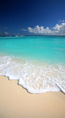 Clear turquoise water lapping at a white sandy beach with blue sky and clouds.