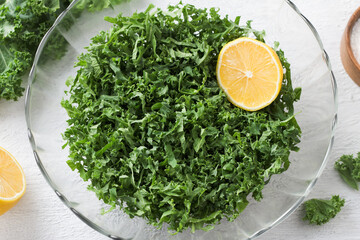 Wall Mural - Chopped kale cabbage leaves with lemon in a transparent bowl on a light gray background