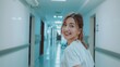 © VK Studio - A nurse smiles warmly as she glances back while walking down a brightly lit hospital hallway.