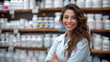 © angellodeco - Female pharmacist in white coat smiling in front of shelves full of products in a pharmacy. Smiling female pharmacist posing in pharmacy with shelves of products behind
