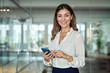 © NullByte Store - Happy mature professional business woman using cell phone at office, portrait. Smiling mid age 45 years old businesswoman executive standing at work lobby holding smartphone looking at camera.