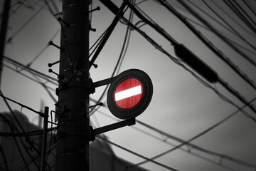 A bold red prohibition sign commands attention atop a utility pole, surrounded by an intricate maze of overhead wires, hinting at urban life as twilight settles in.