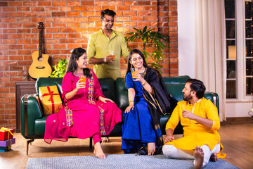 Cheerful Indian couples and friends celebrating Diwali at home with drinks, sweets, taking selfies