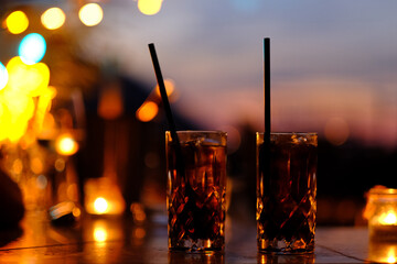 Refreshing alcoholic cocktail cuba libra in a glass with  ice cubes, on dark sunset background